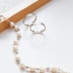 A delicate arrangement of pearl necklace and silver rings on the pages of an open book, exuding elegance.